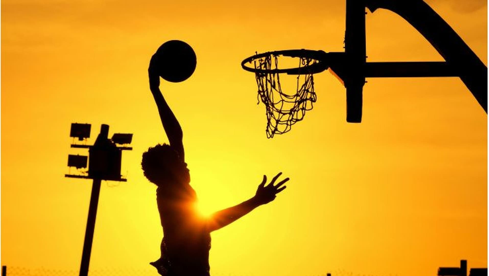 Student-athlete leaping toward the basketball hoop at golden hour